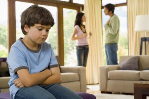 A child in-focus slouching in the foreground with parents arguing out-of-focus in the background