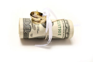 Wedding rings tied with ribbon to rolled-up hundred dollar bills